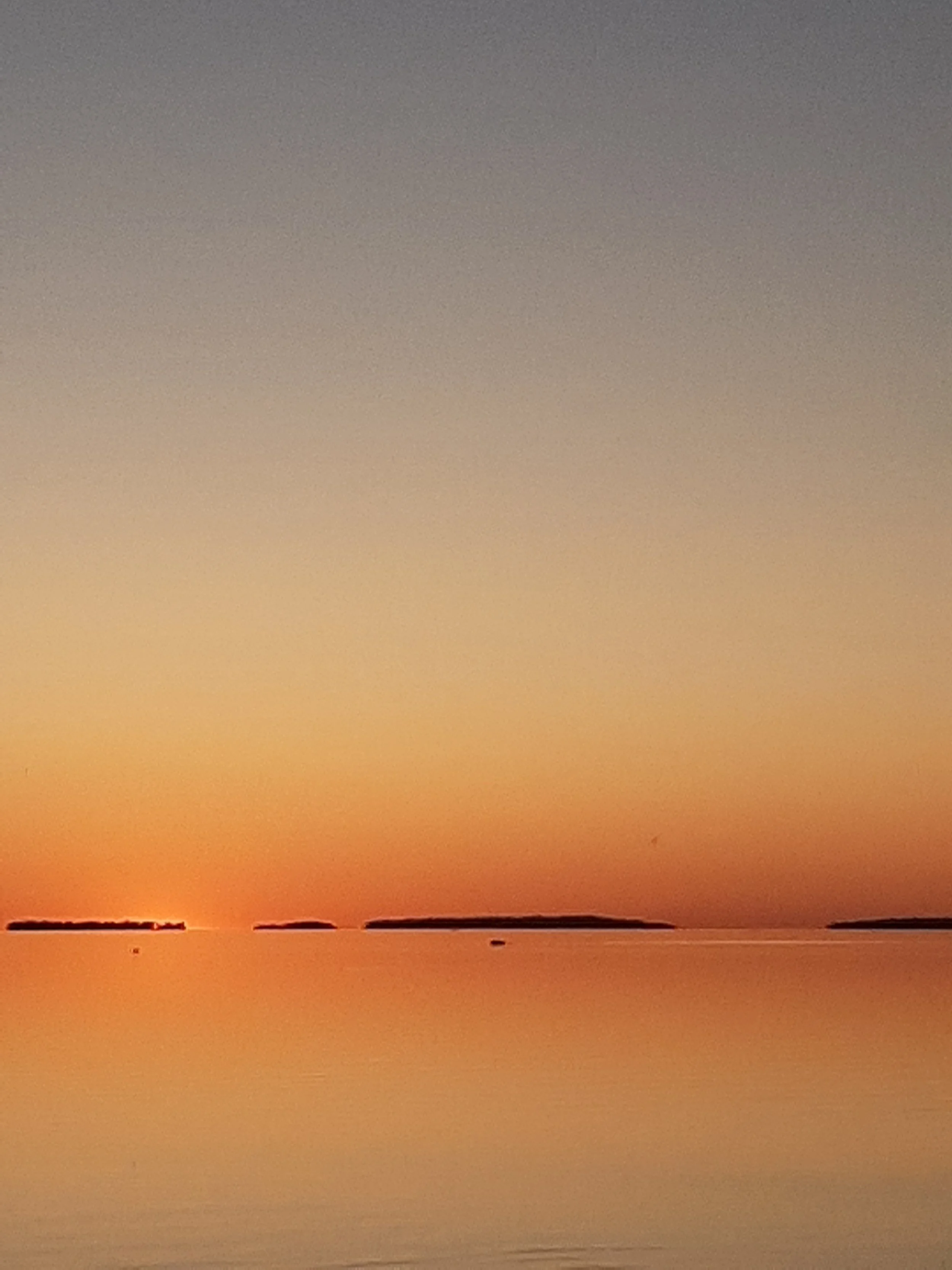 Sunset over a calm body of water with small islands in the distance.