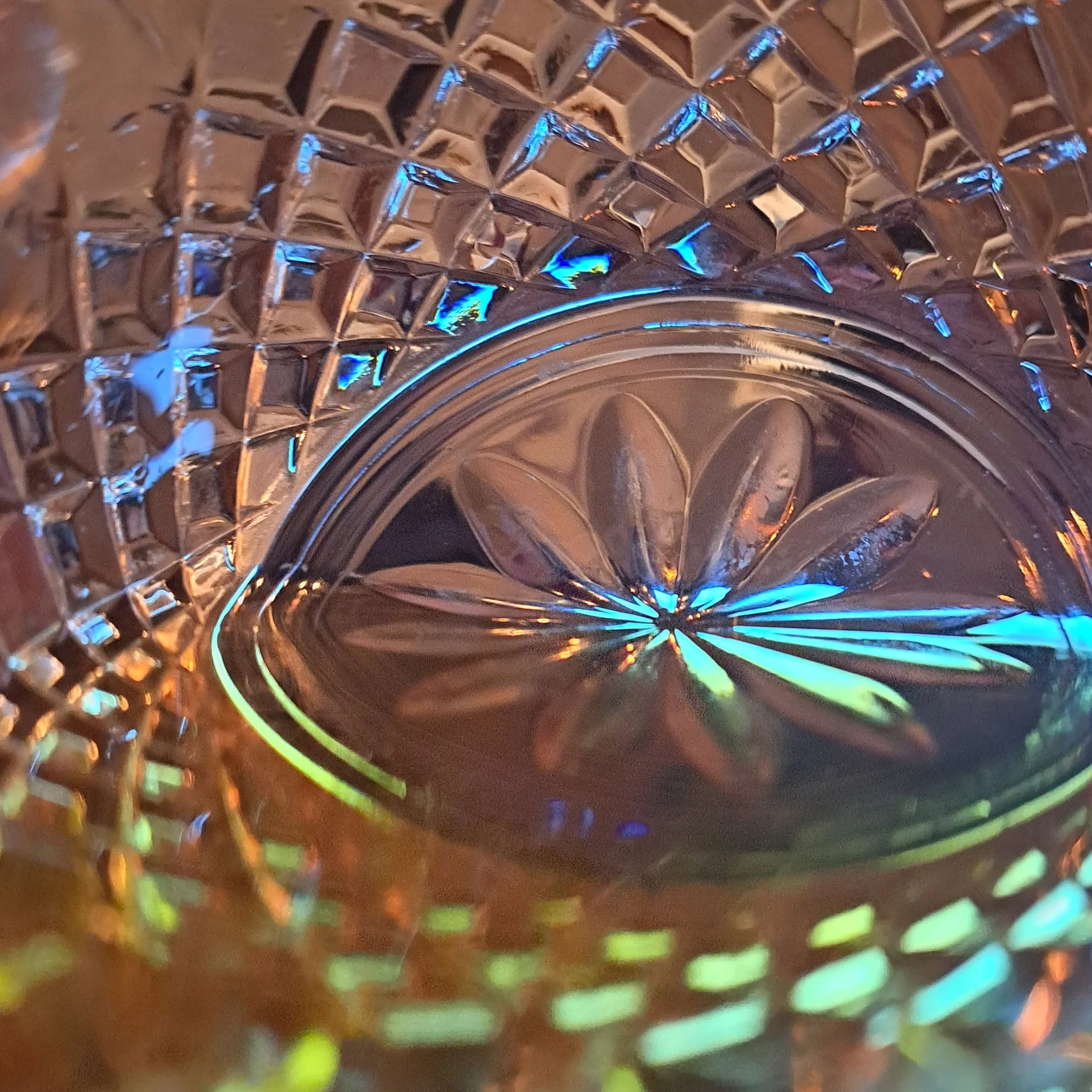Close-up of a cut glass with intricate diamond and floral patterns, reflecting colorful light.