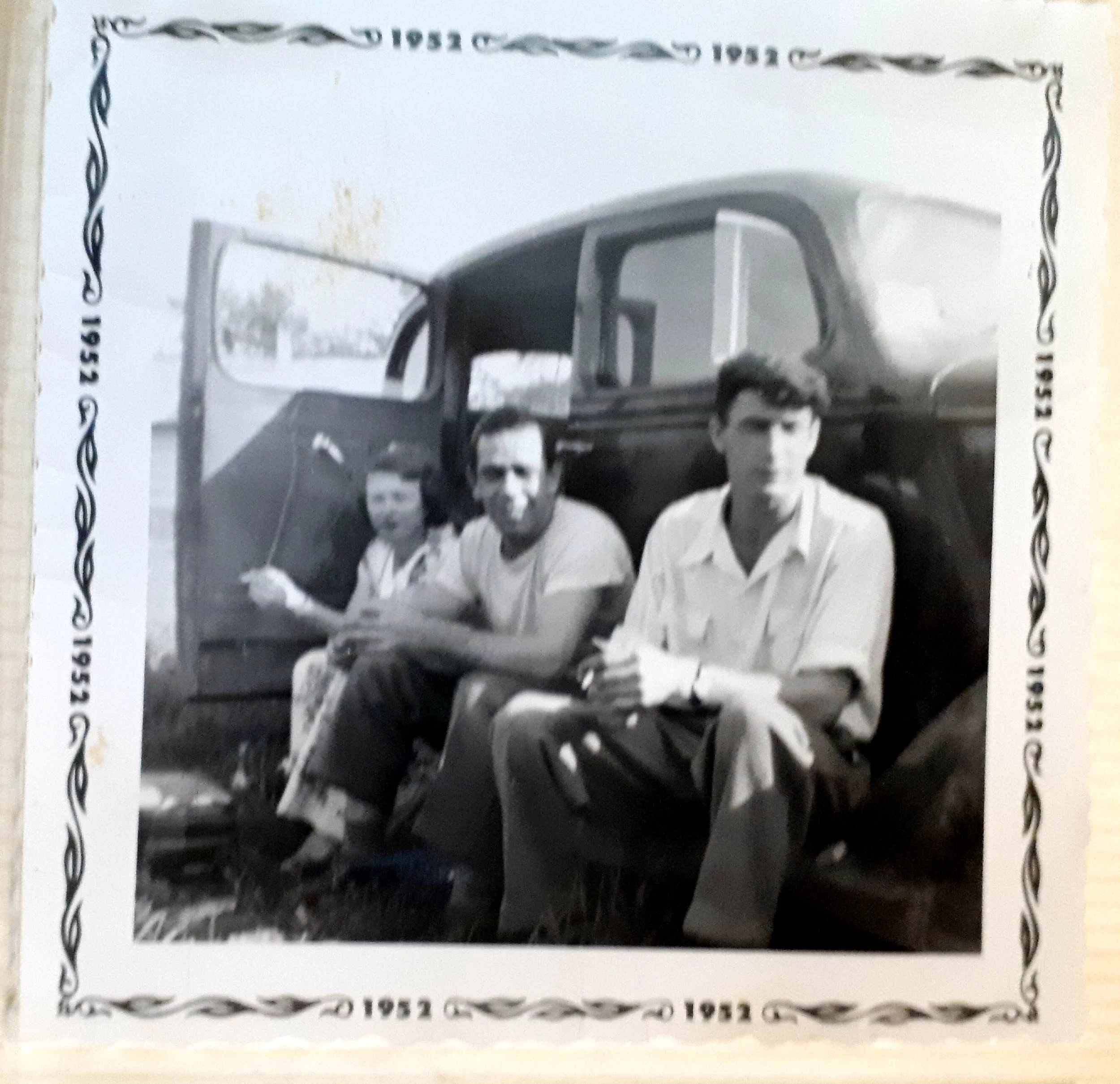 Black-and-white photo of three young men sitting on a vintage truck, with a decorative border and the year 1952 printed around the edges.
