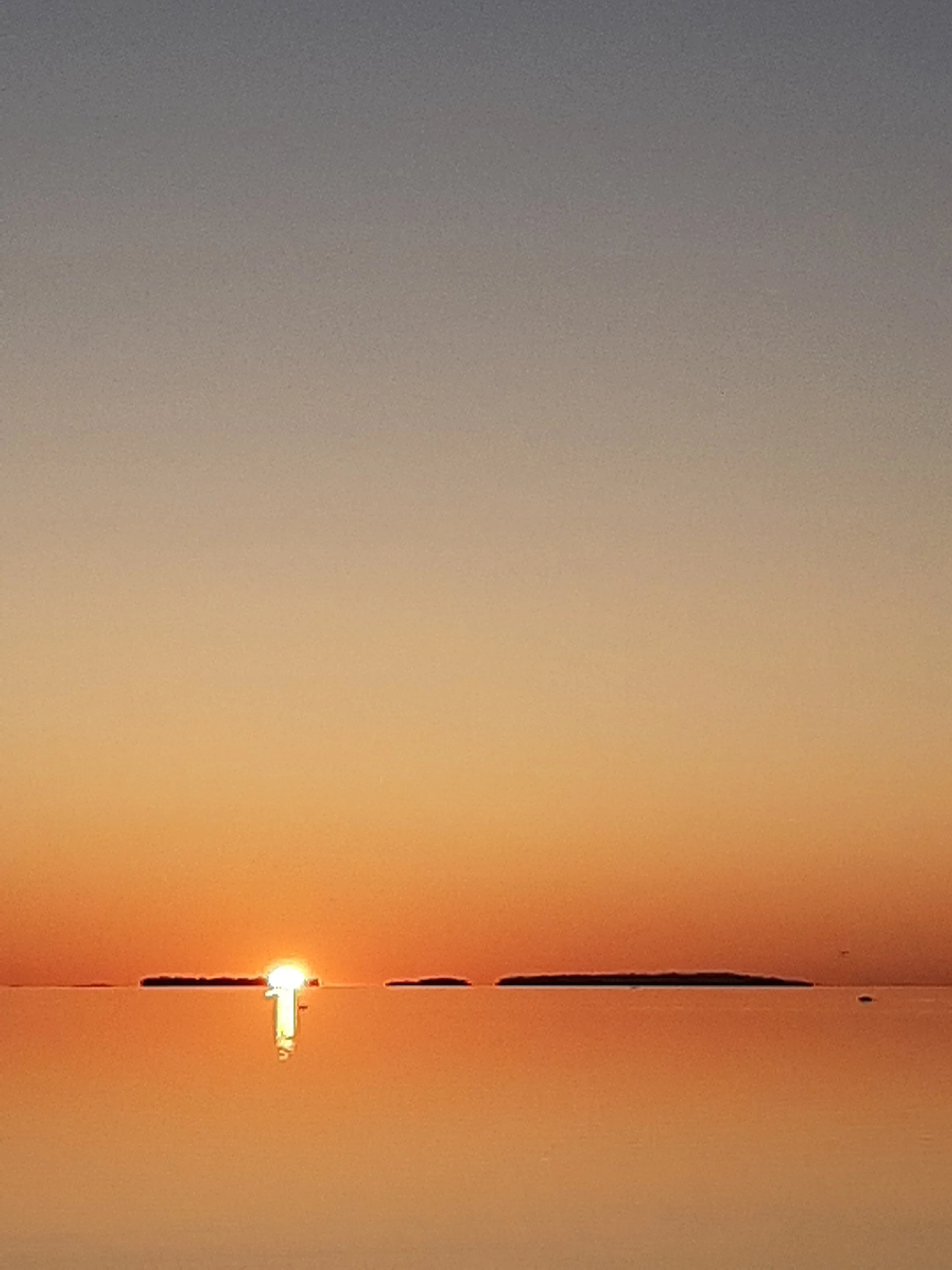 Sun setting over a calm body of water with a small island in the distance.