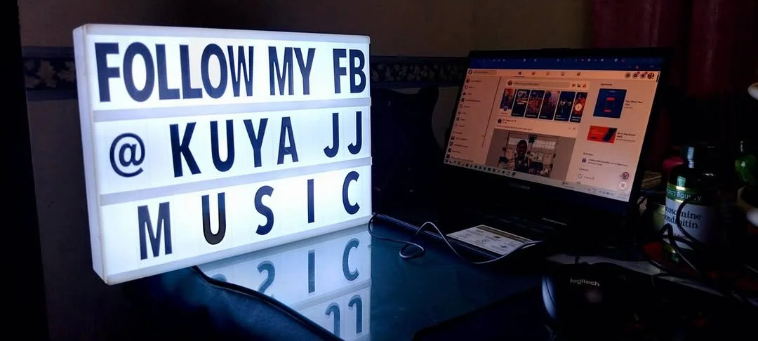 Illuminated sign advertising to follow a Facebook page @KuyaaJJ for music.