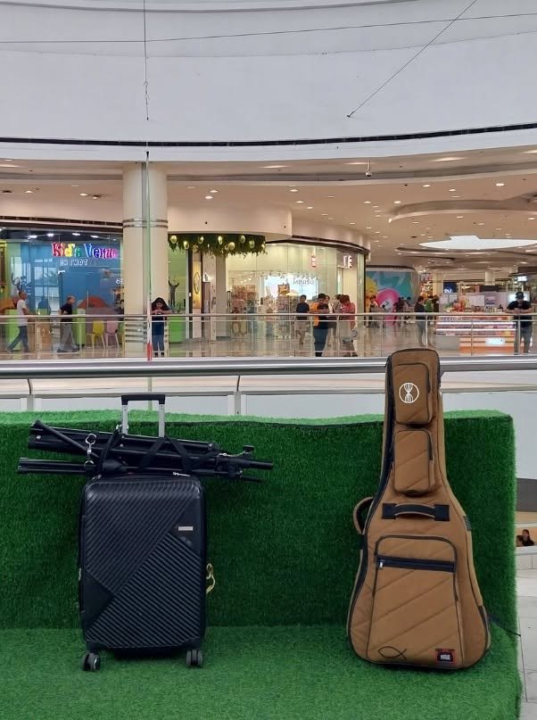 Luggage and a guitar case on a green surface in a shopping mall.