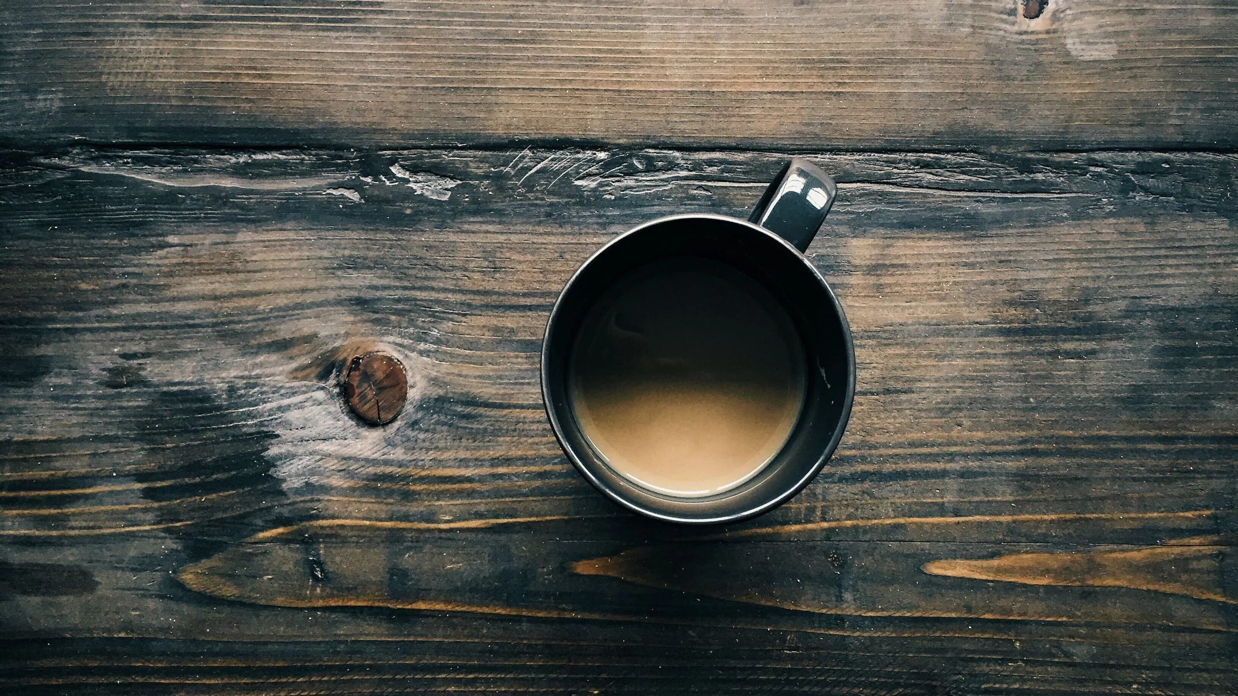 Top-down view of a black mug filled with coffee on a rustic wooden table.