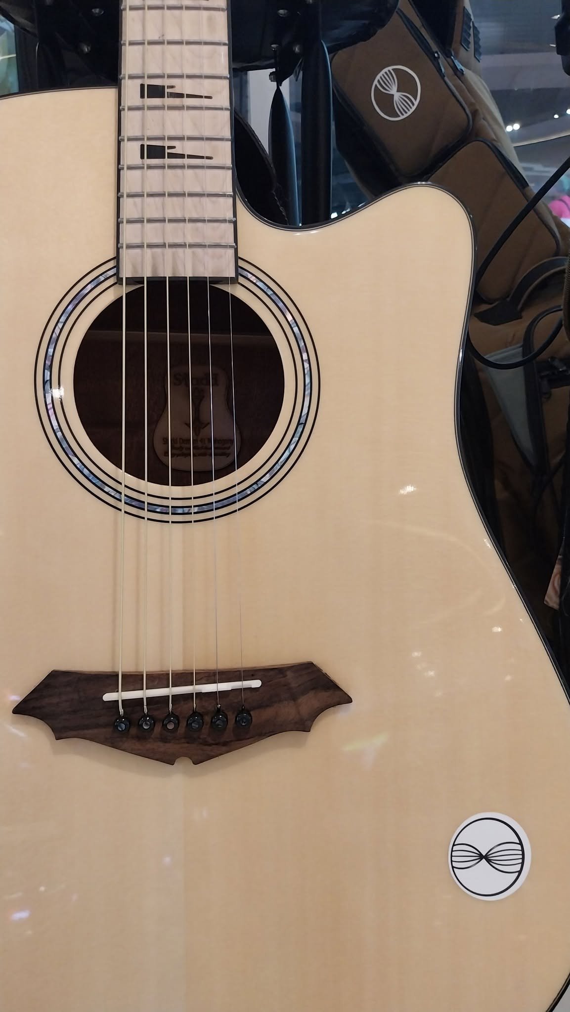 An acoustic guitar with a natural wood finish on a beige surface, with a black sound hole surrounded by a decorative inlay, and a bridge made of darker wood.
