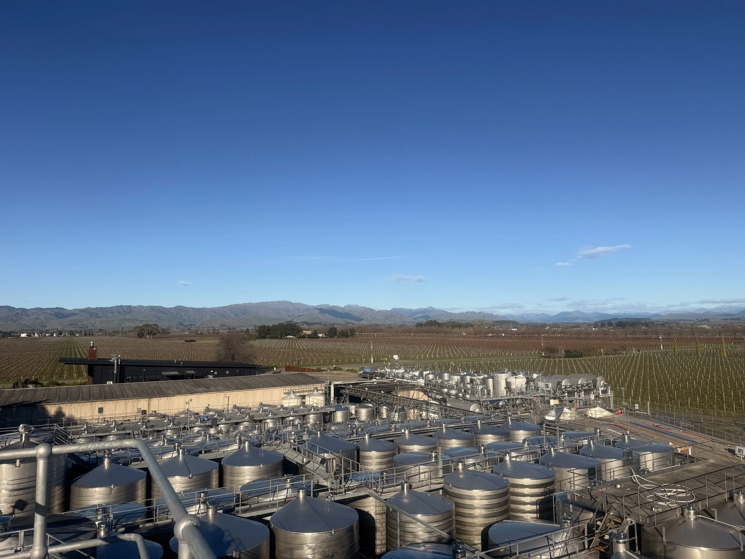Wine tanks on a vineyard, and mountains in the background under a clear blue sky.