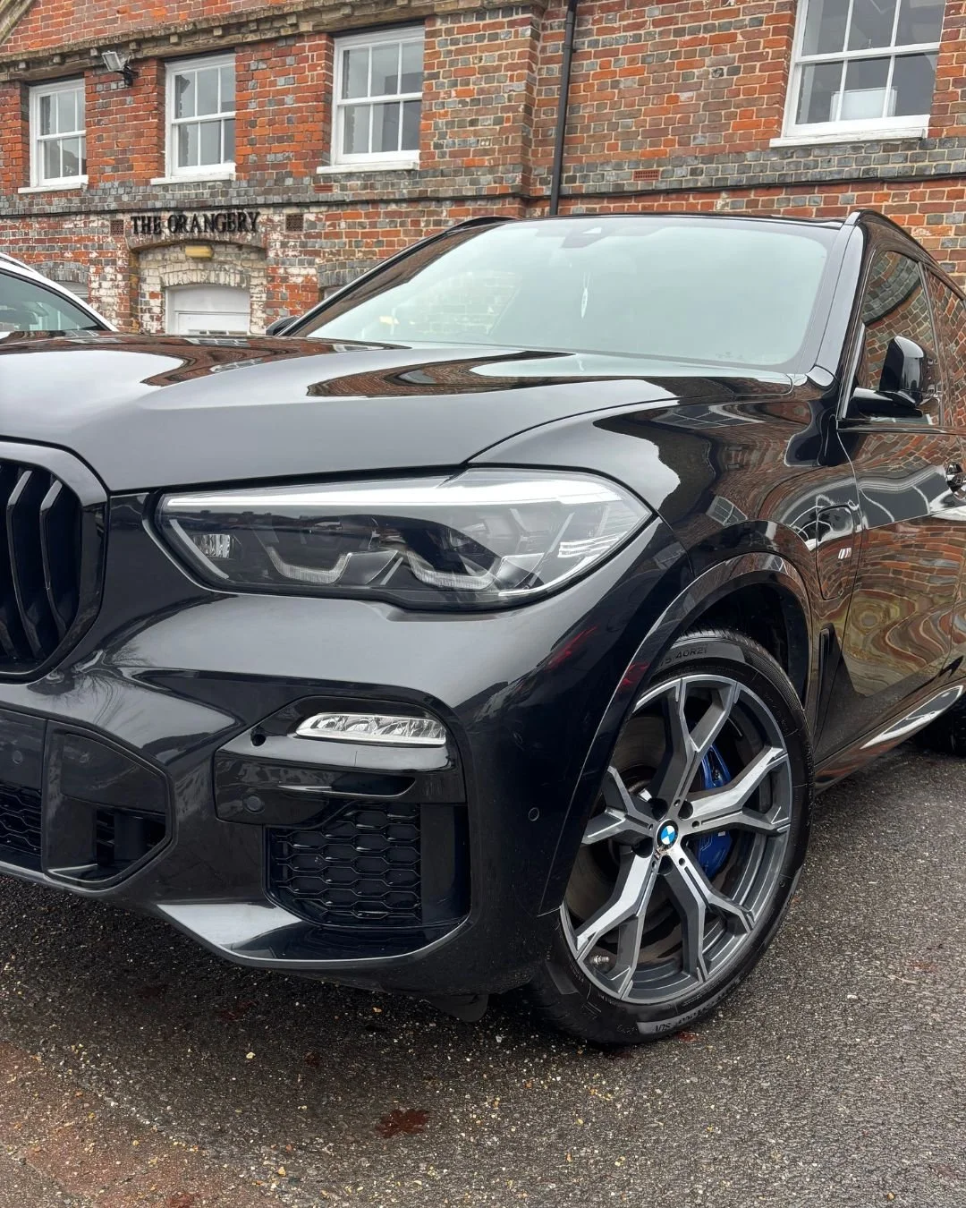 Black BMW SUV parked on a gravel driveway with brick buildings in the background.