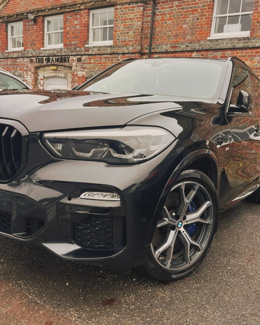 Close-up of a black BMW SUV parked on a cobblestone street in front of a brick building with white window frames.