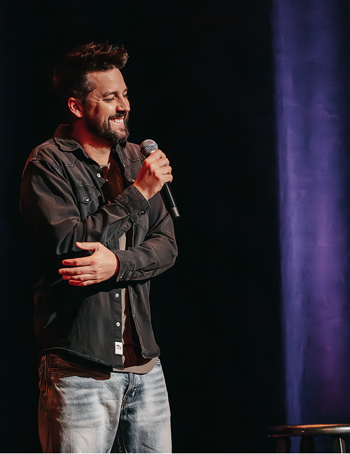 john crist on stage wearing a leather coat and faded jeans with a purple light