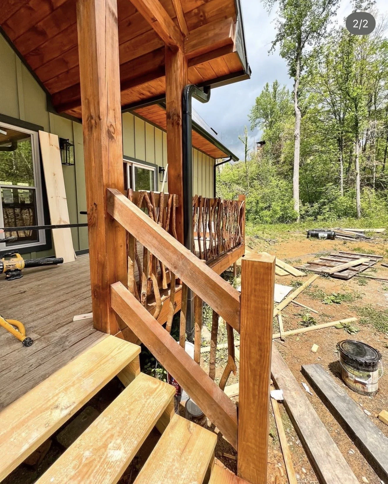 Handcrafted twig railing detail along an outdoor cabin deck surrounded by forest.