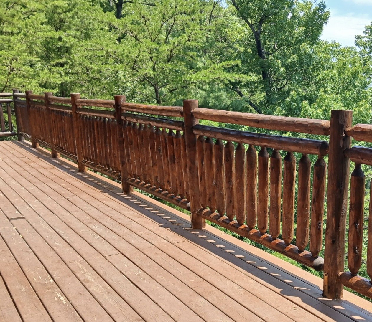 Rustic timber railing with smooth round spindles on a covered cabin porch in the mountains.