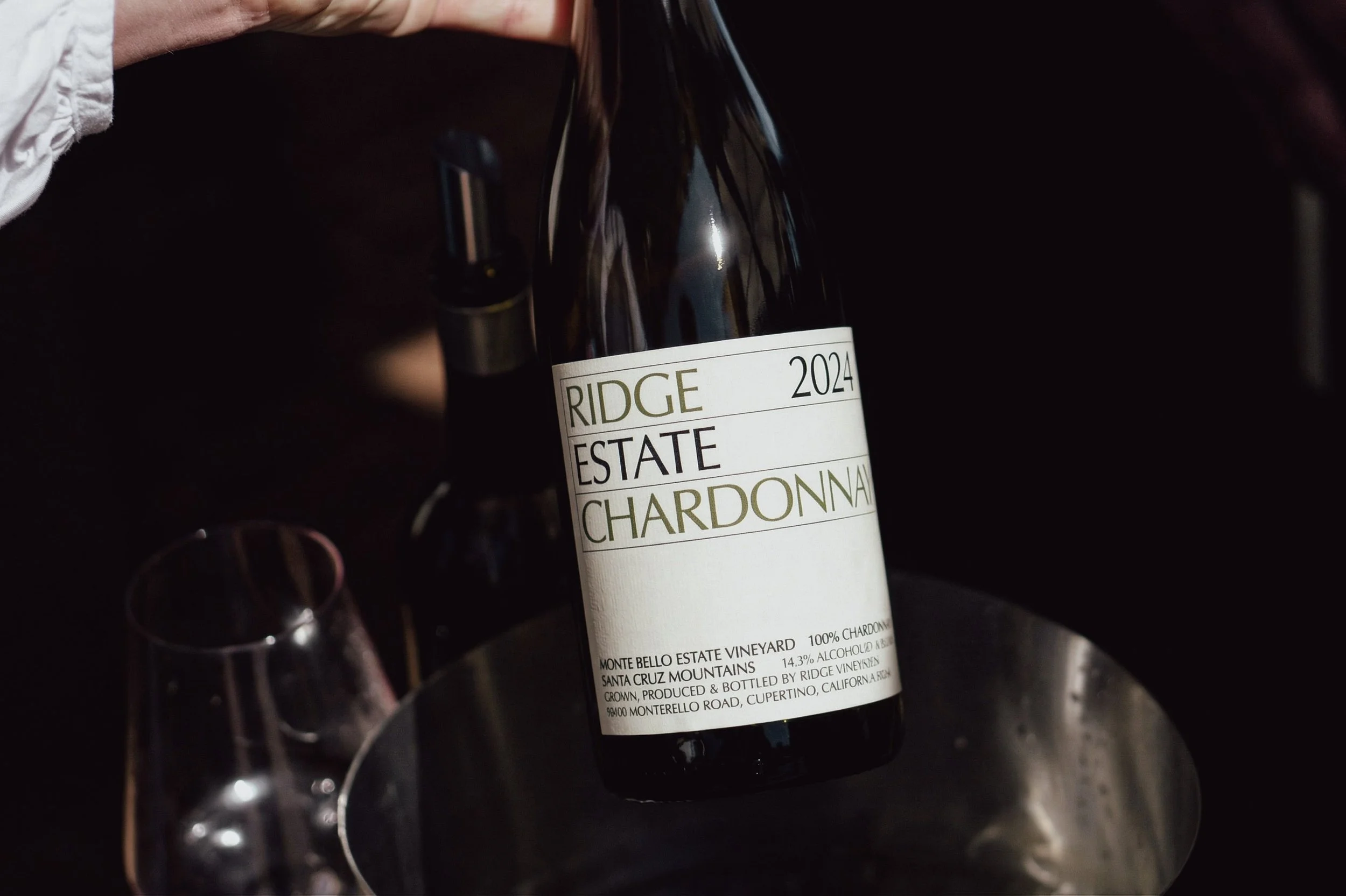 A wine bottle labeled 'Ridge 2024 Estate Chardonnay' being placed in a bucket with a wine glass nearby.