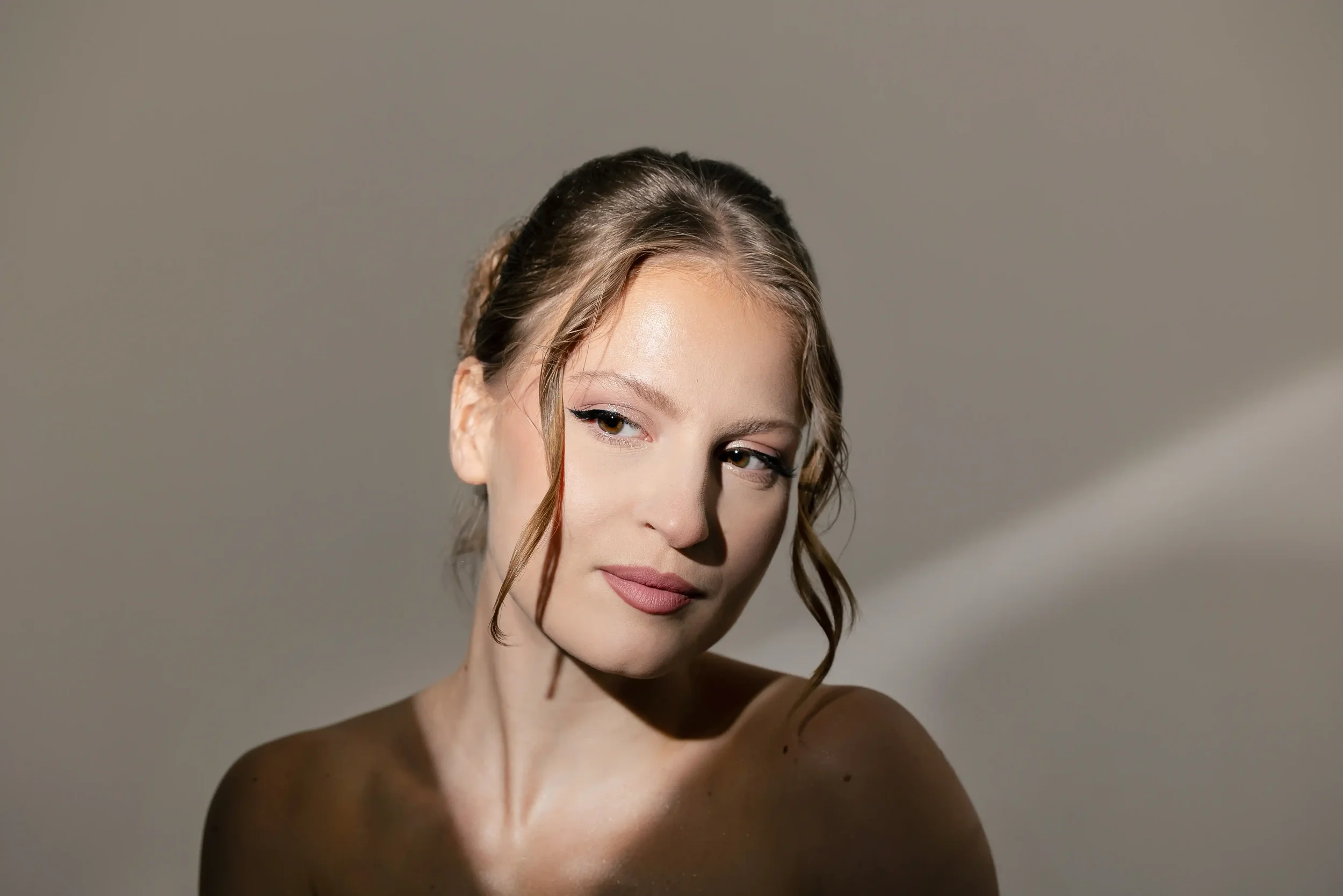 Portrait d'une femme aux cheveux bouclés, regardant légèrement sur le côté, avec un éclairage doux, contre un fond gris