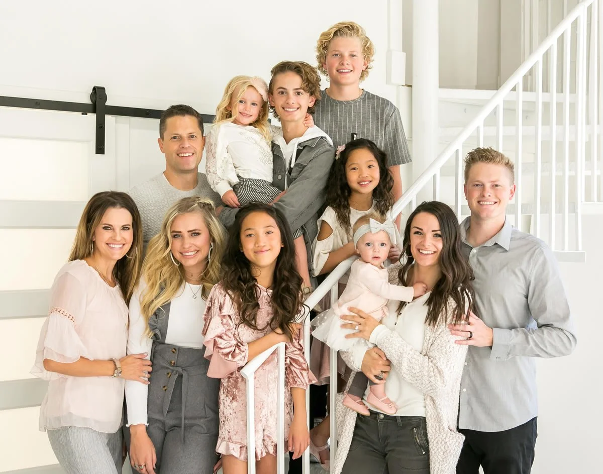 Dr. Russel Makenna's family portrait of twelve people, including children and adults, smiling and posing together in a bright room.