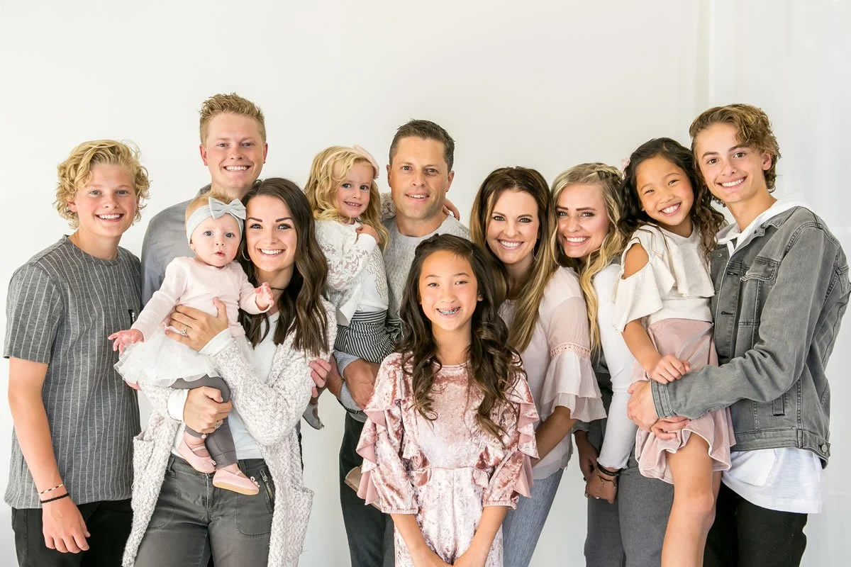 Dr. Russel Makenna's family portrait of twelve people, including children and adults, smiling and posing together in a bright room.