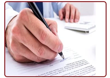 A person signing a document with a pen at a desk.
