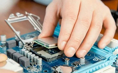 A person's hand installing a CPU onto a blue computer motherboard.