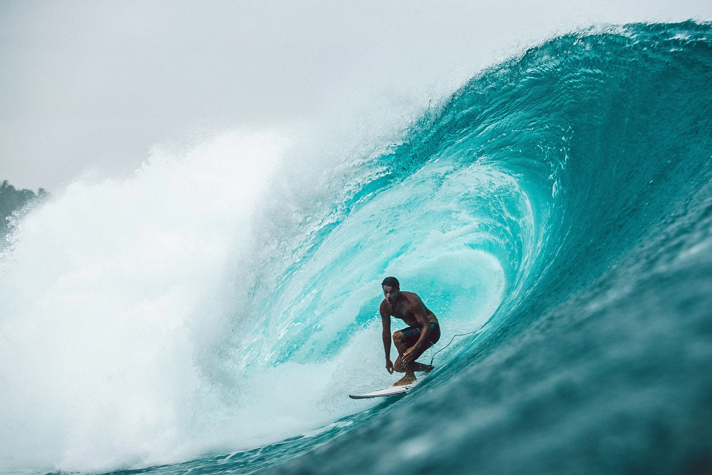 A male surfer riding inside a large blue ocean wave.