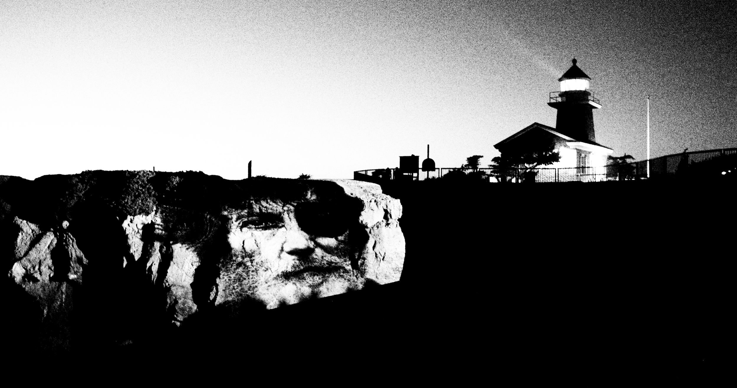 A black and white photo of Mount Rushmore with a lighthouse in the background.