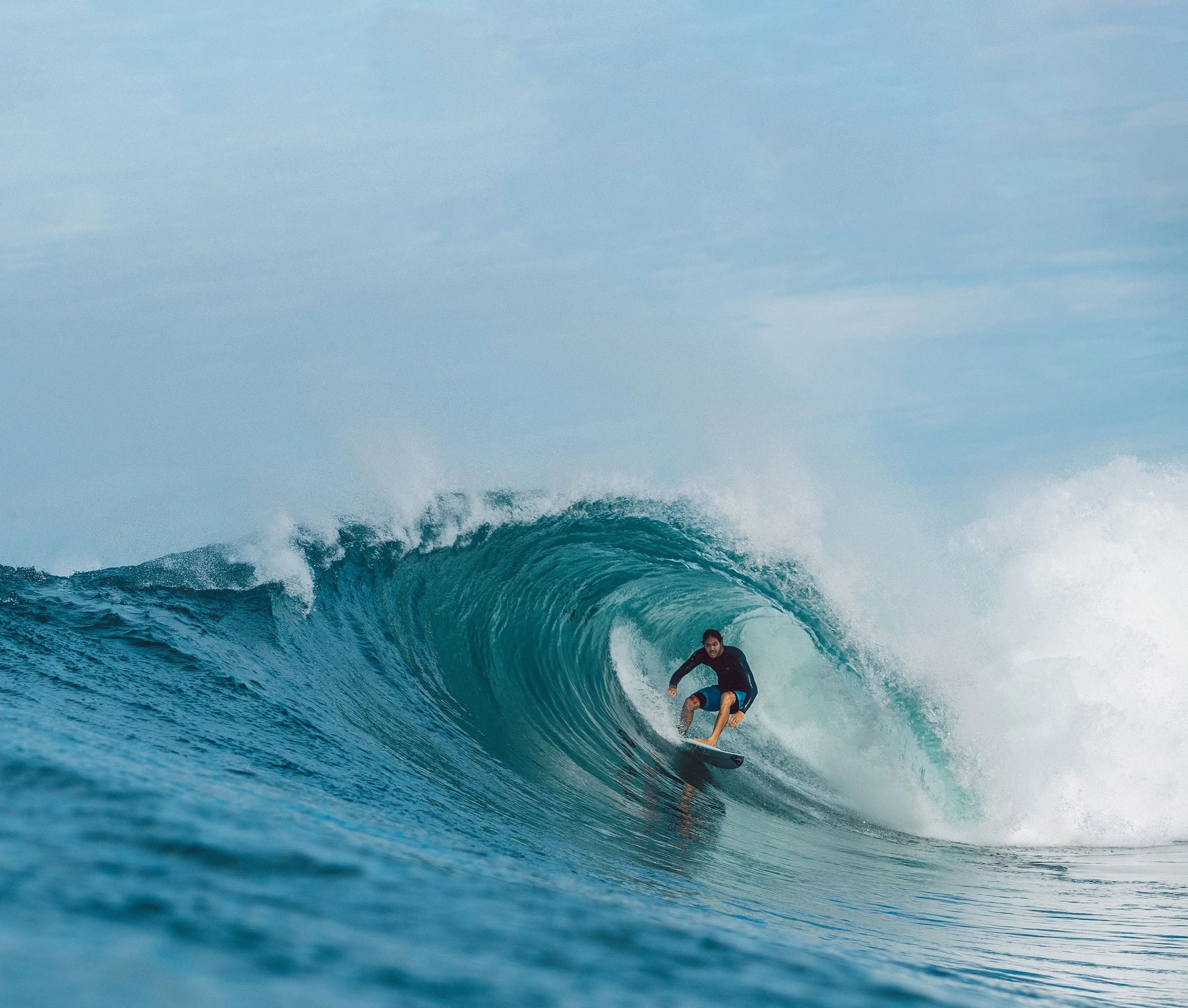 A person surfing on a large wave in the ocean under a cloudy sky.