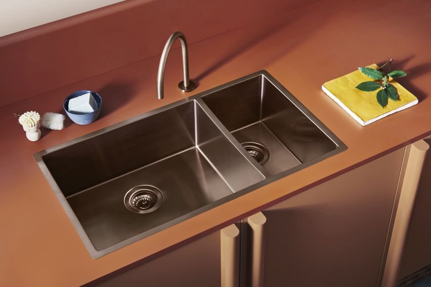 A kitchen sink with two basins, a faucet, and small items on the countertop, including a blue bowl, a sponge, and a plant on a yellow cloth.