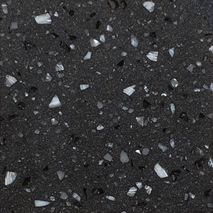 Close-up of a black Staron Terrazzo Siena solid surface with scattered shiny gray and white fragments.