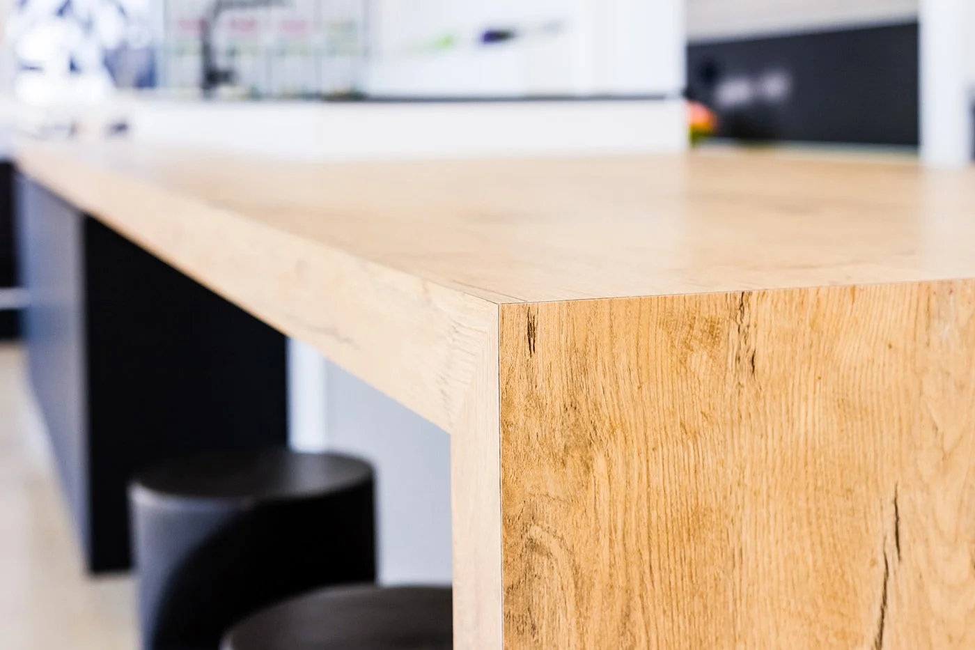 Close-up of a timber laminated table with a natural finish and visible wood grain, with black chairs visible underneath