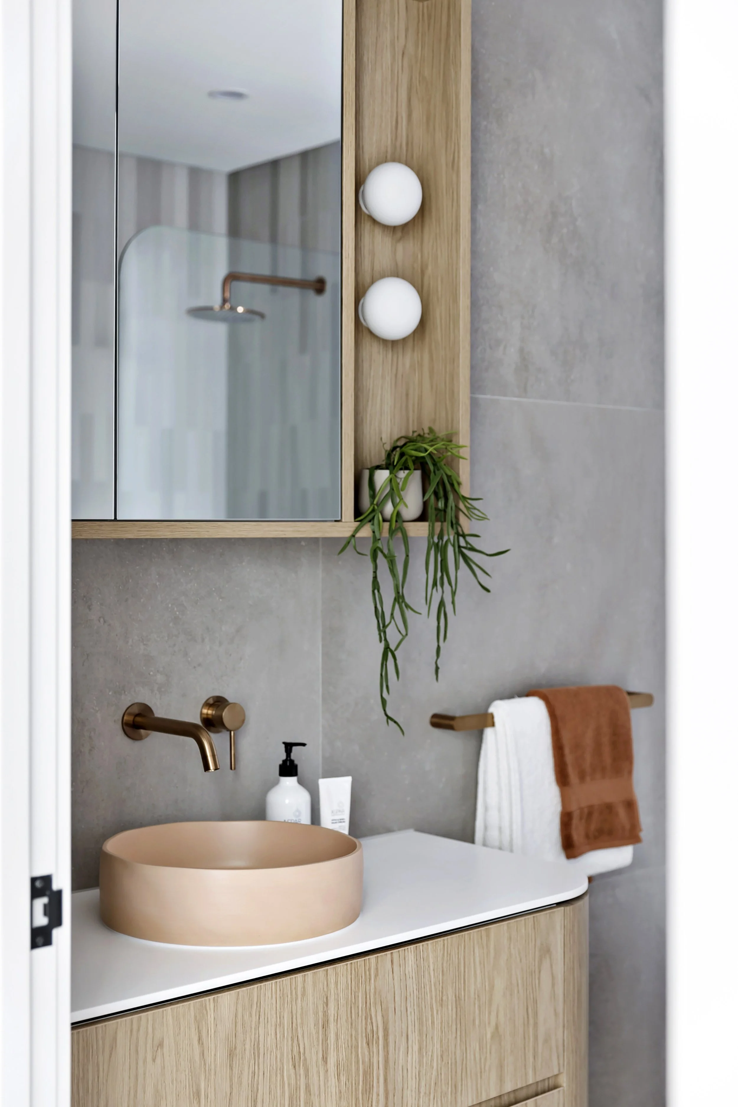 A modern corian glacier white bathroom vanity with a peach-colored vessel sink, a black soap dispenser, a small tube, and a gold towel bar with white and brown towels. 