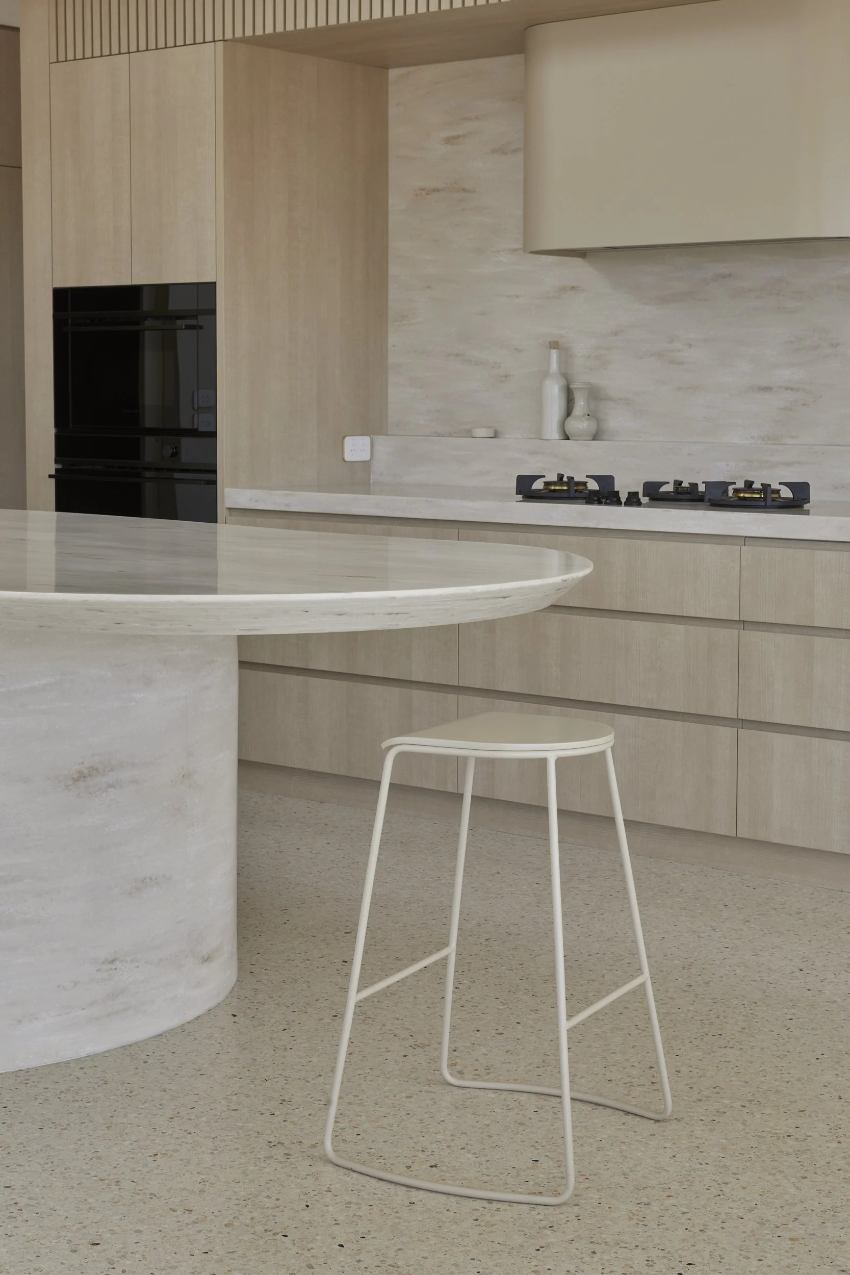 A minimalist kitchen with light wood cabinets, a corian witch hazel island benchtop and a modern white bar stool.