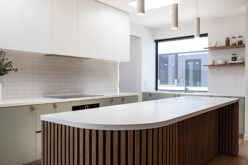 Modern kitchen with white cabinets, a corian glacier white countertop, a curved kitchen island with vertical wooden slats, a window with black trim, open shelves with jars and bowls, and white subway tile backsplash.