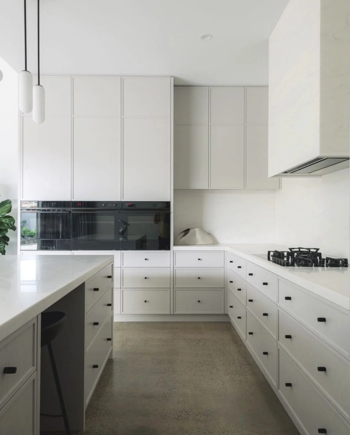 Modern corian venaro white kitchen with black cabinet handles, a built-in oven, gas stove, and minimal decor, including a large plant and a white decorative object.