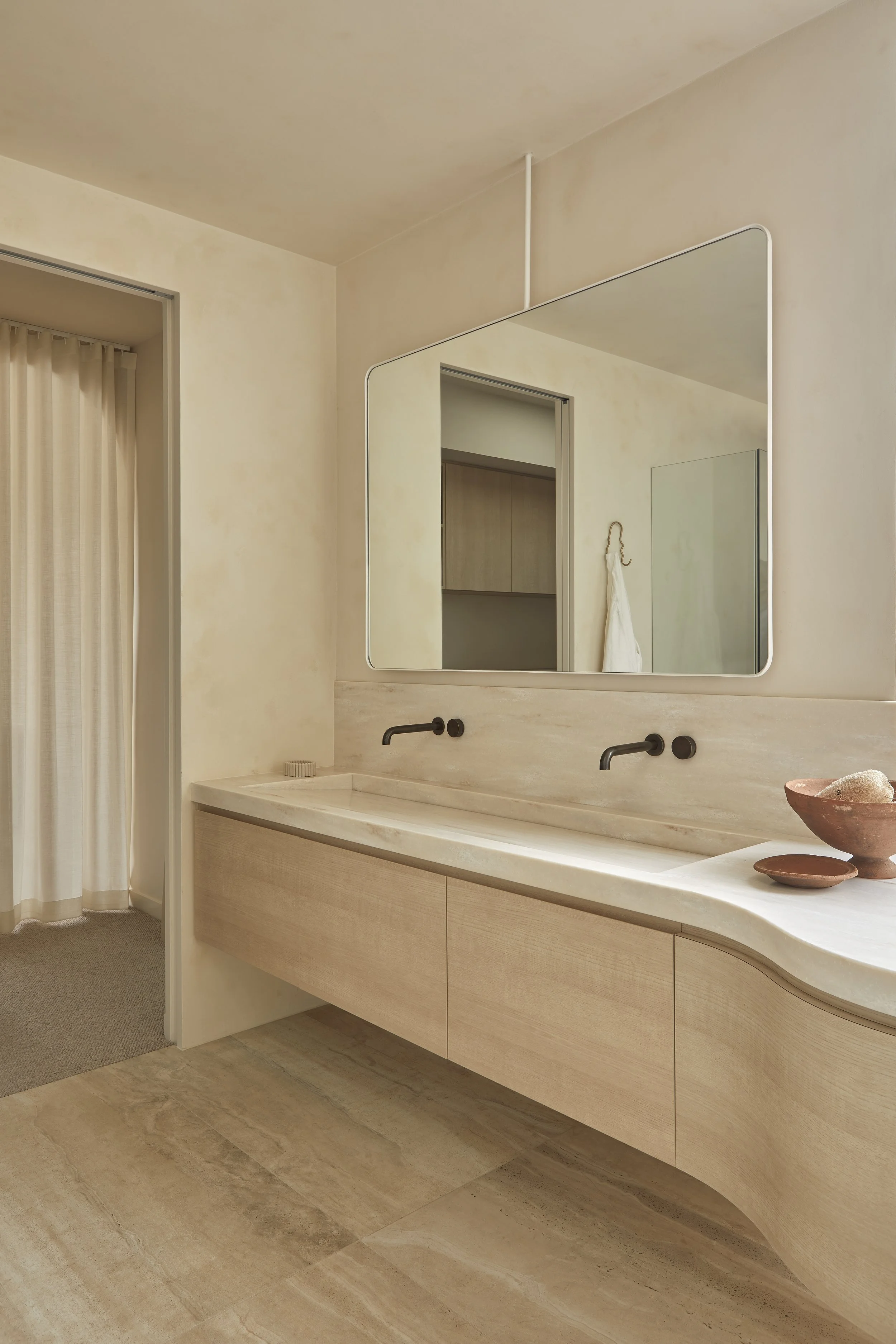 Modern bathroom with Corian Witch Hazel benchtops and large mirror, gunmetal wall-mounted faucets, and decorative bowls on the counter.