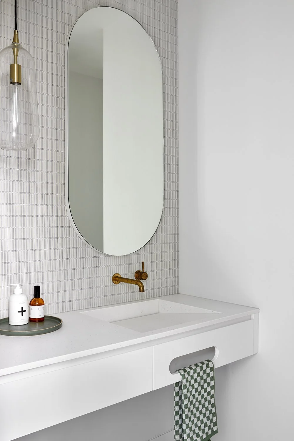Modern bathroom with a Corian Glacier White vanity with integrated basin, oval mirror, brass faucet, and wall-mounted glass pendant light.