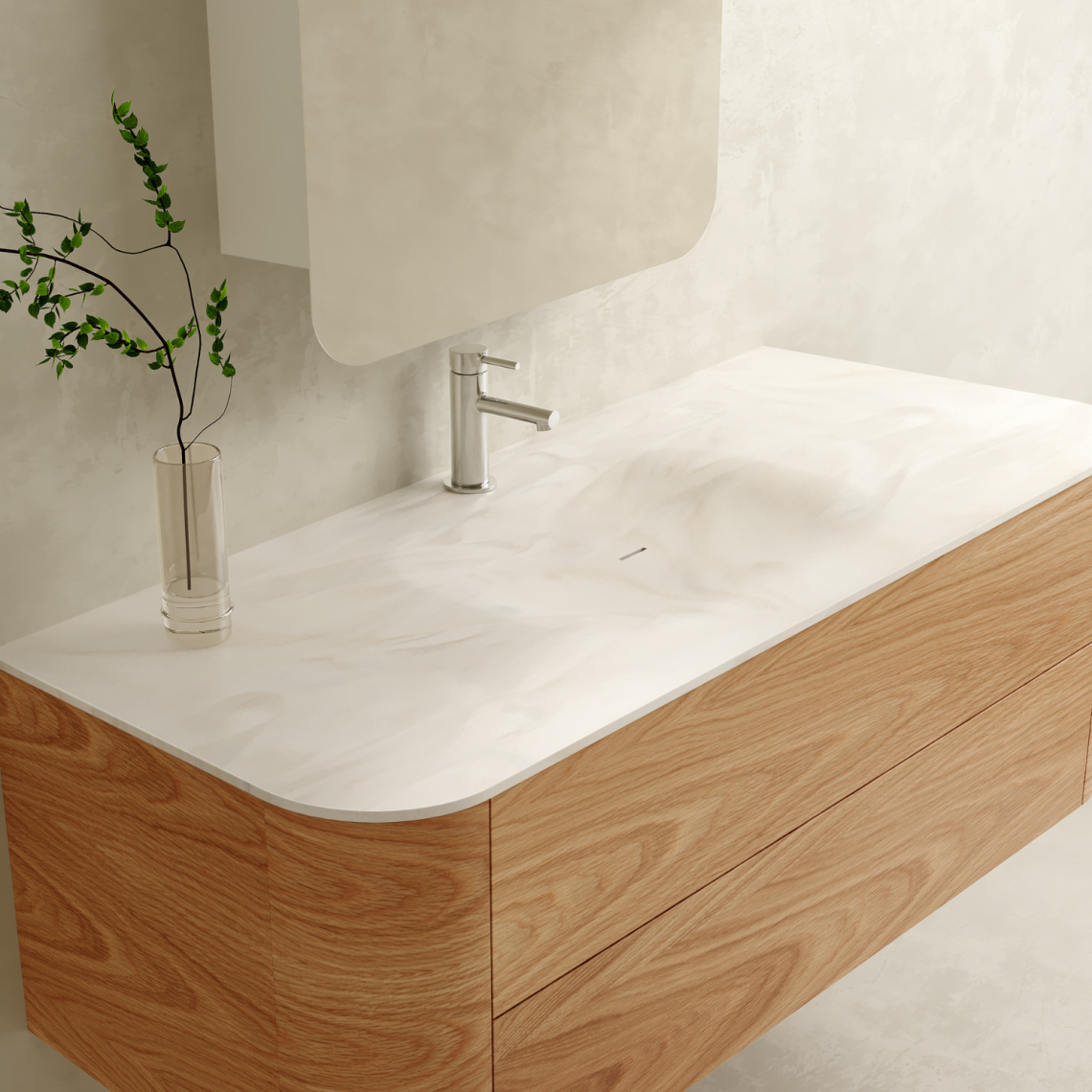 Bathroom vanity with a white marble sink, a modern silver faucet, a tall glass vase with green leafy branches, and a light-colored wall in the background.