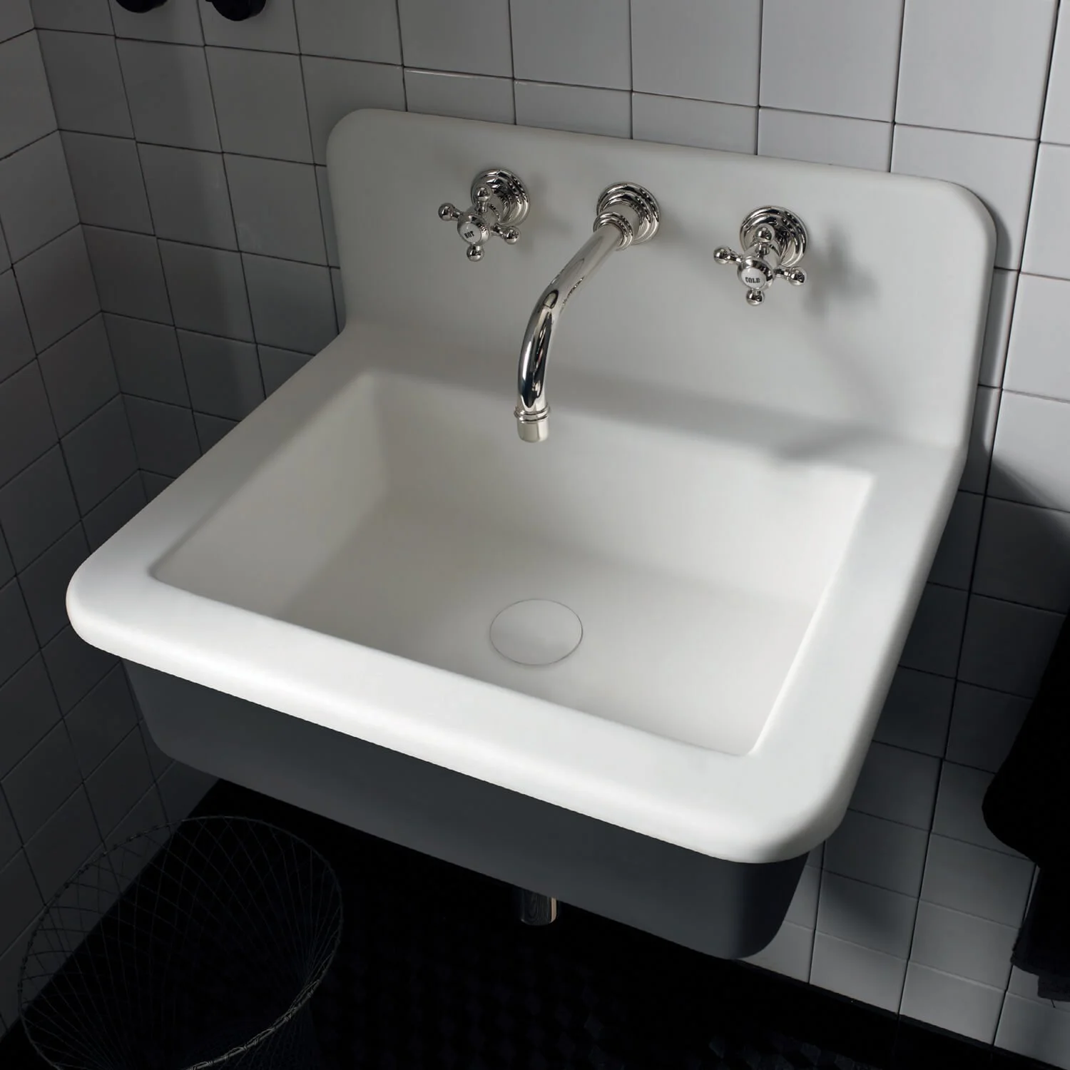 A white Corian basin attached to a tiled wall, with chrome hot and cold water taps and a central spout.