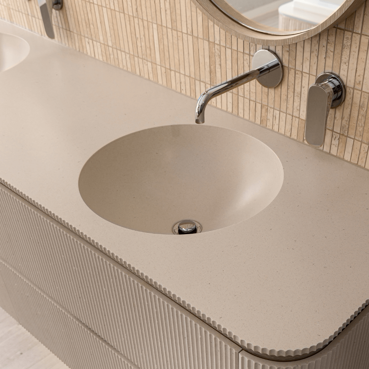 A modern bathroom sink with a beige countertop, integrated round basin, a chrome faucet, and a beige tiled wall with a mirror above.