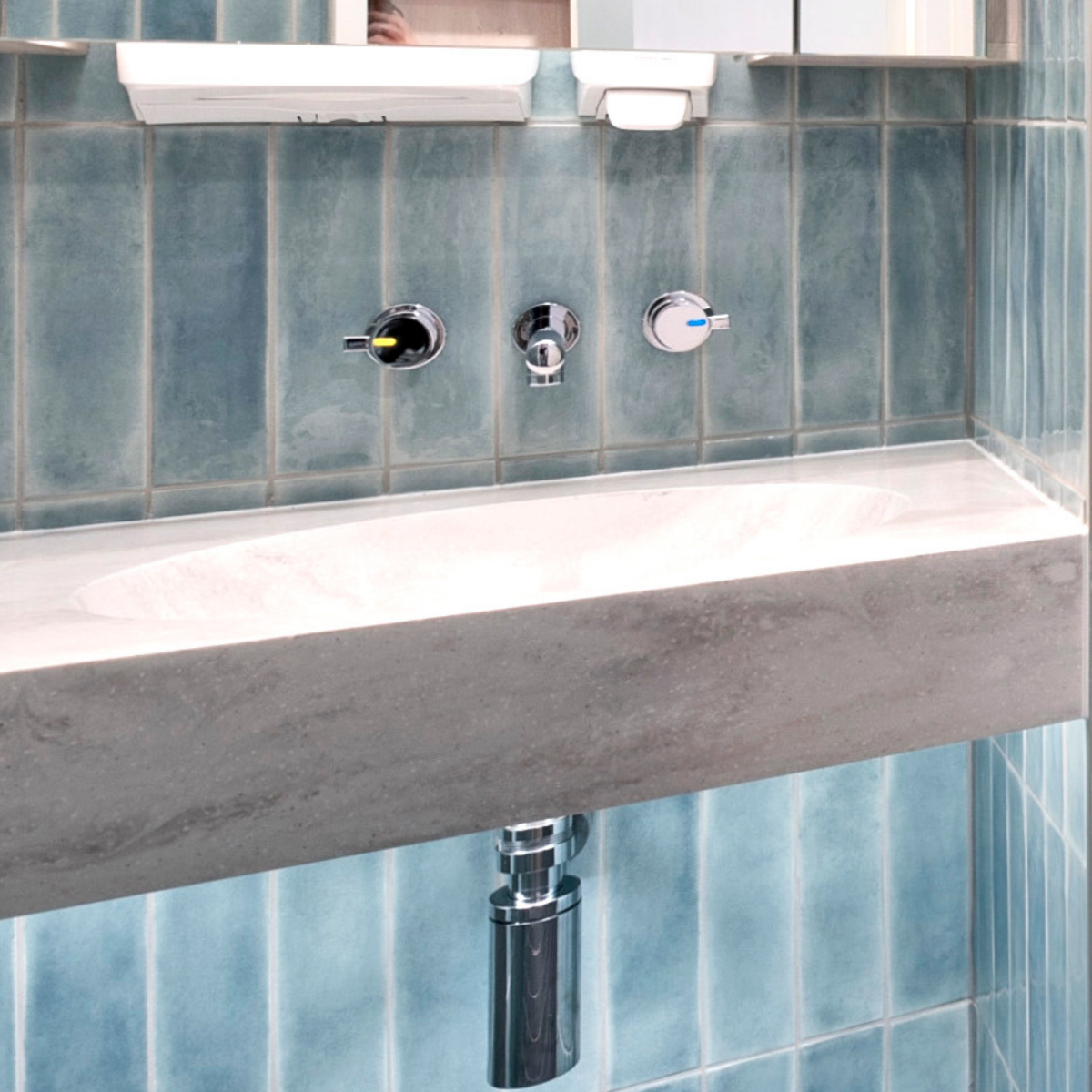 A bathroom sink with three chrome fixtures and a mirror above it, set against blue tiled walls.