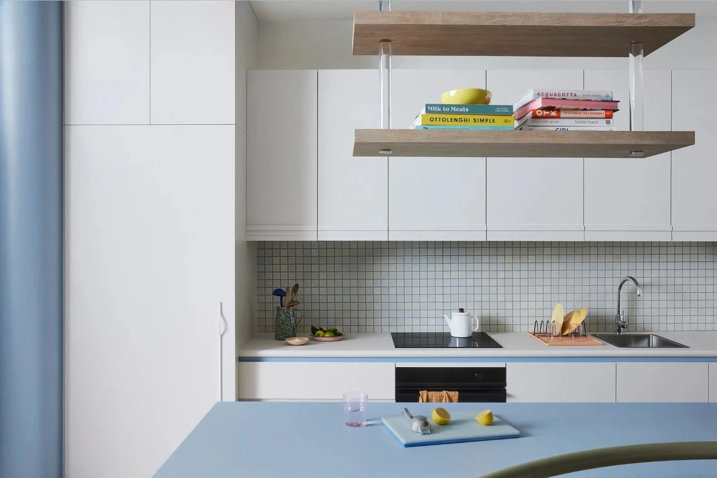 Modern kitchen with white cabinets, a gray countertop, a small sink, and two floating shelves with books and a yellow bowl.