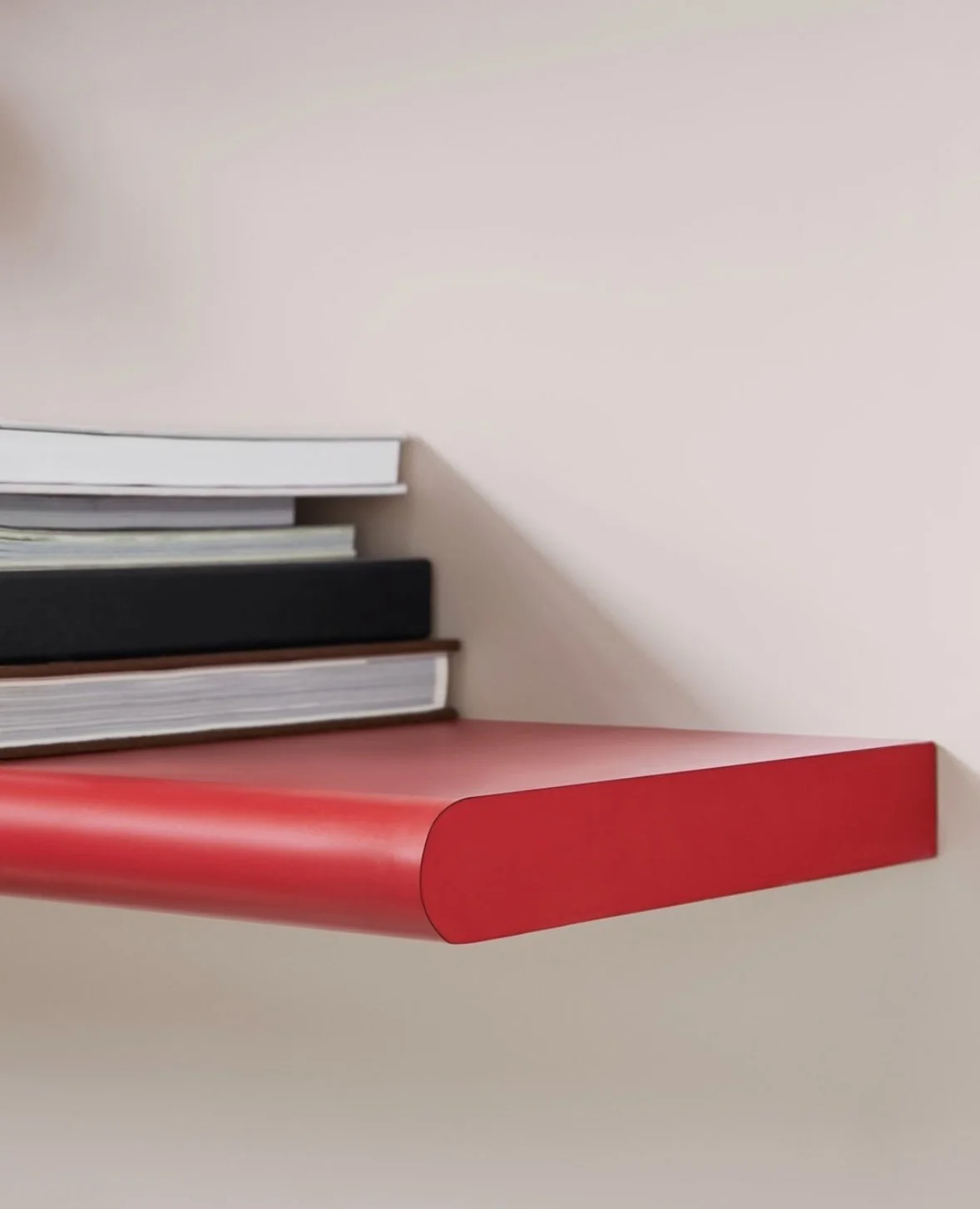 A close-up of a pink wall-mounted bookshelf with several books stacked horizontally.