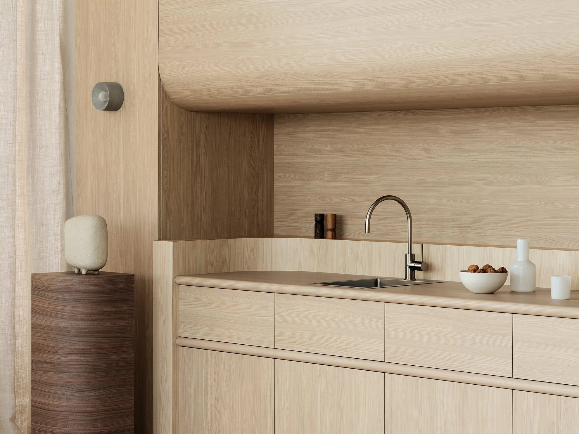 Minimalist kitchen with light wood cabinetry, small items like a bowl of walnuts, a white vase, and a candle on the countertop.