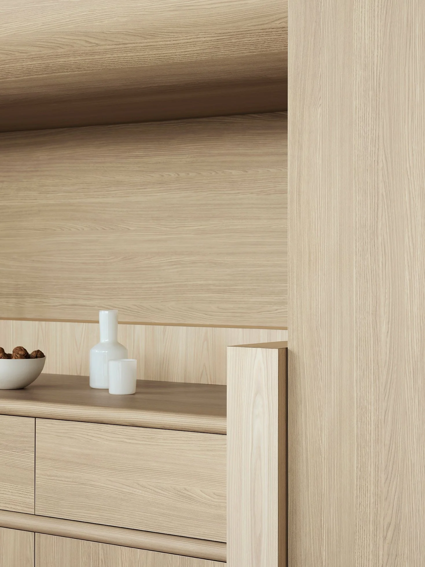 Close-up of a light wood dresser and wall with a white bowl of walnuts and white ceramic vases placed on top.