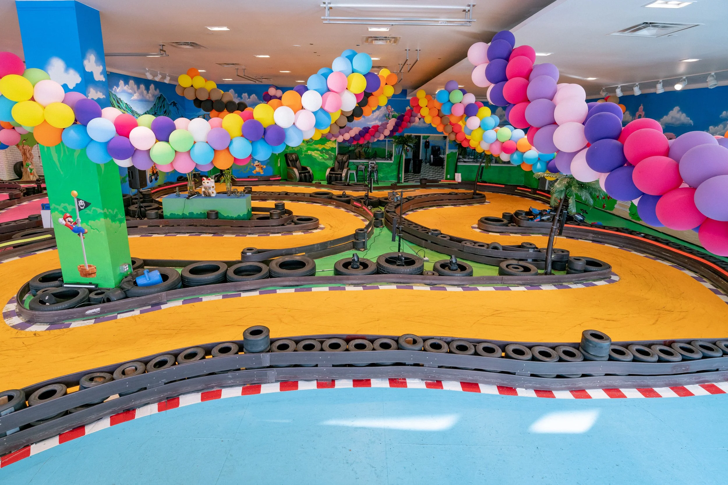 Indoor go-kart track decorated with colorful balloons and cartoon-themed mural walls.