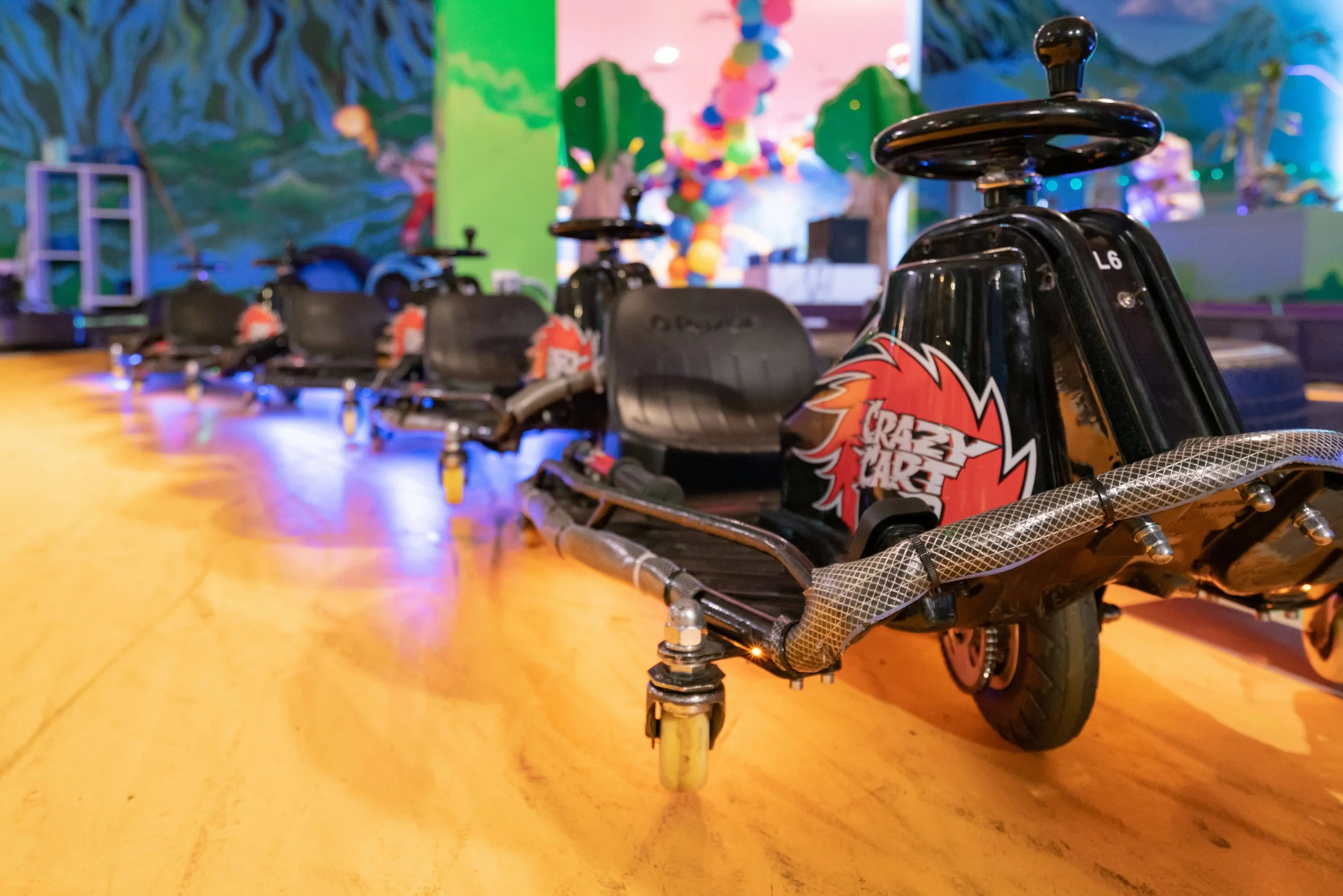 Row of black go-karts with red and white flame decals in an indoor amusement center with colorful murals and decorations.