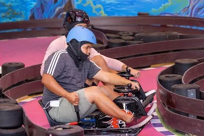 Two people drifting go-karts in tandem at an indoor amusement center.