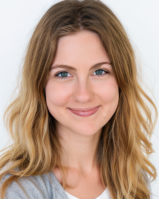 A young woman with long, wavy blonde hair and blue eyes smiling at the camera against a plain light background.