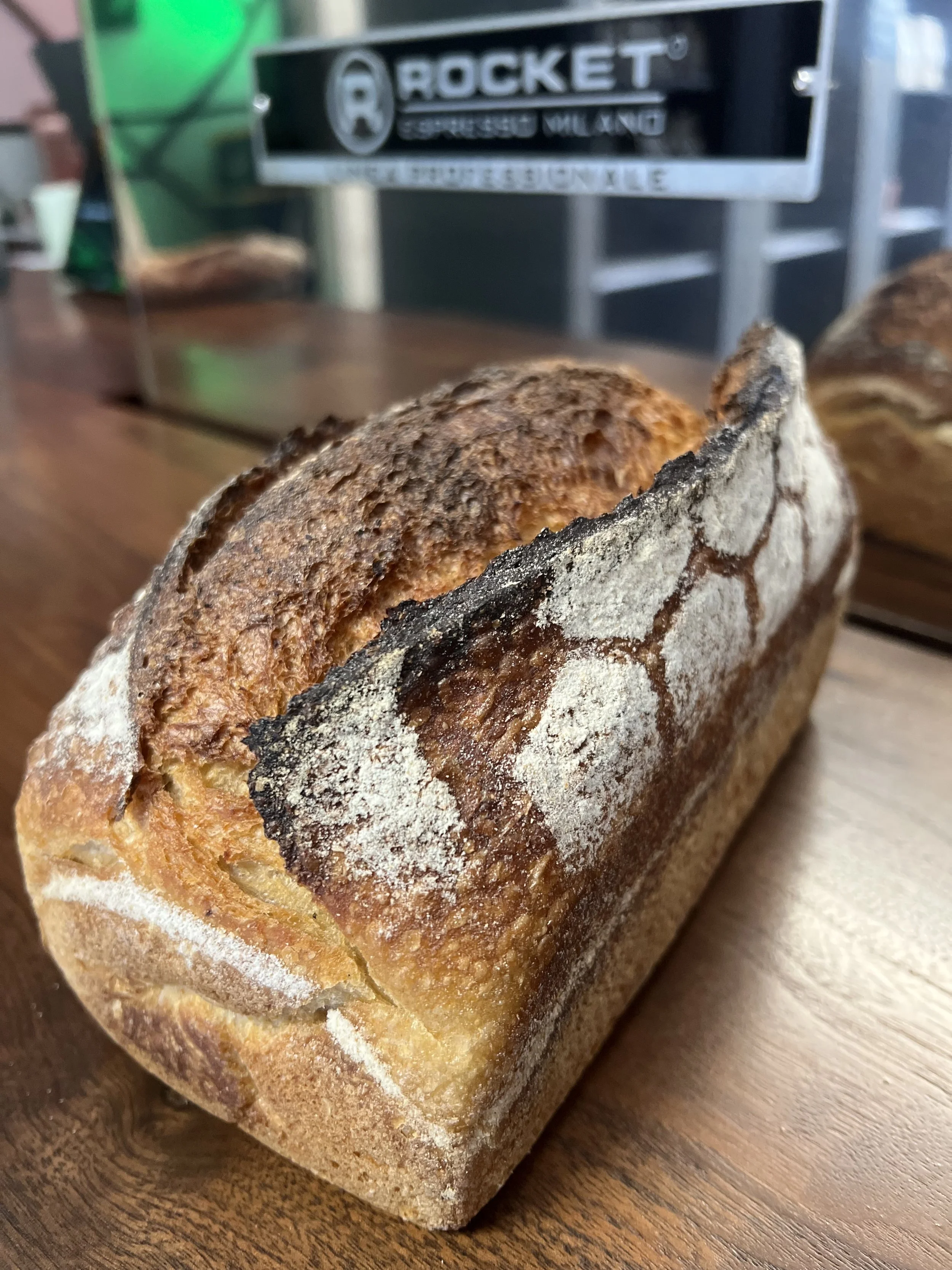 A loaf of rustic, crusty bread with a dusting of flour on a wooden surface.