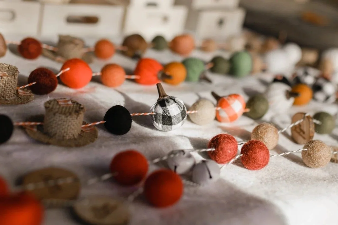 A variety of colorful felt and fabric ball garlands laid out on a surface, with small clothespins and a row of white drawers in the background.
