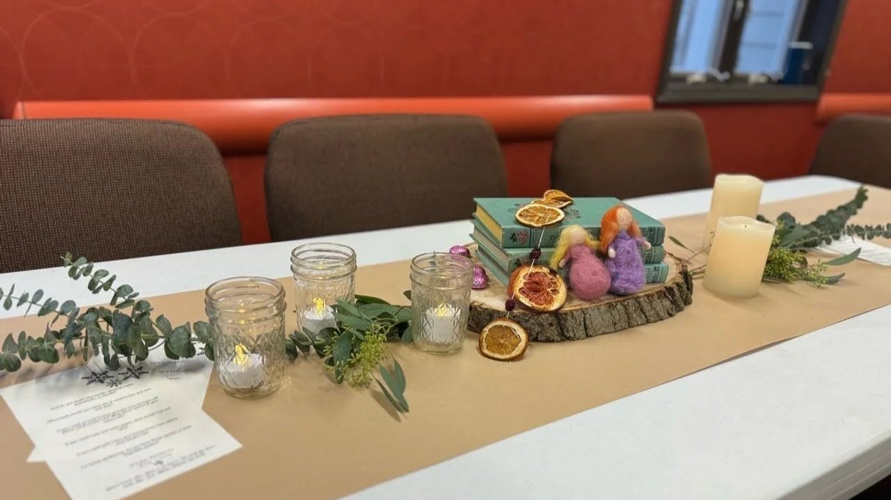 Table decorated with candles, greenery, dried orange slices, and felt birds, with a stack of books on a wooden slab, set up for a cozy event or gathering.