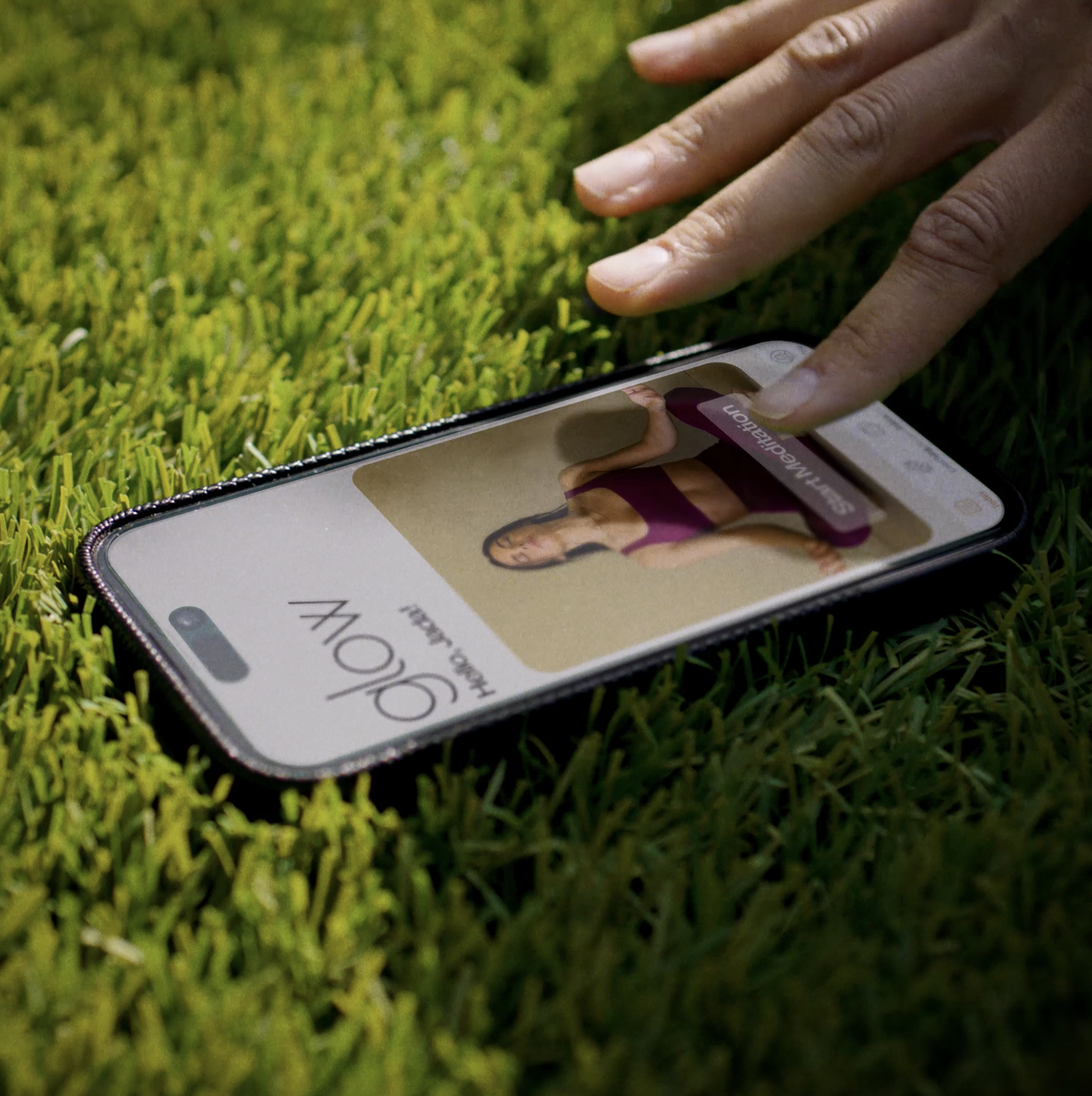 A smartphone lying on grass, displaying a dating profile with a woman in a purple sports bra and black pants, and the words "CALV" and "Happy and" visible.