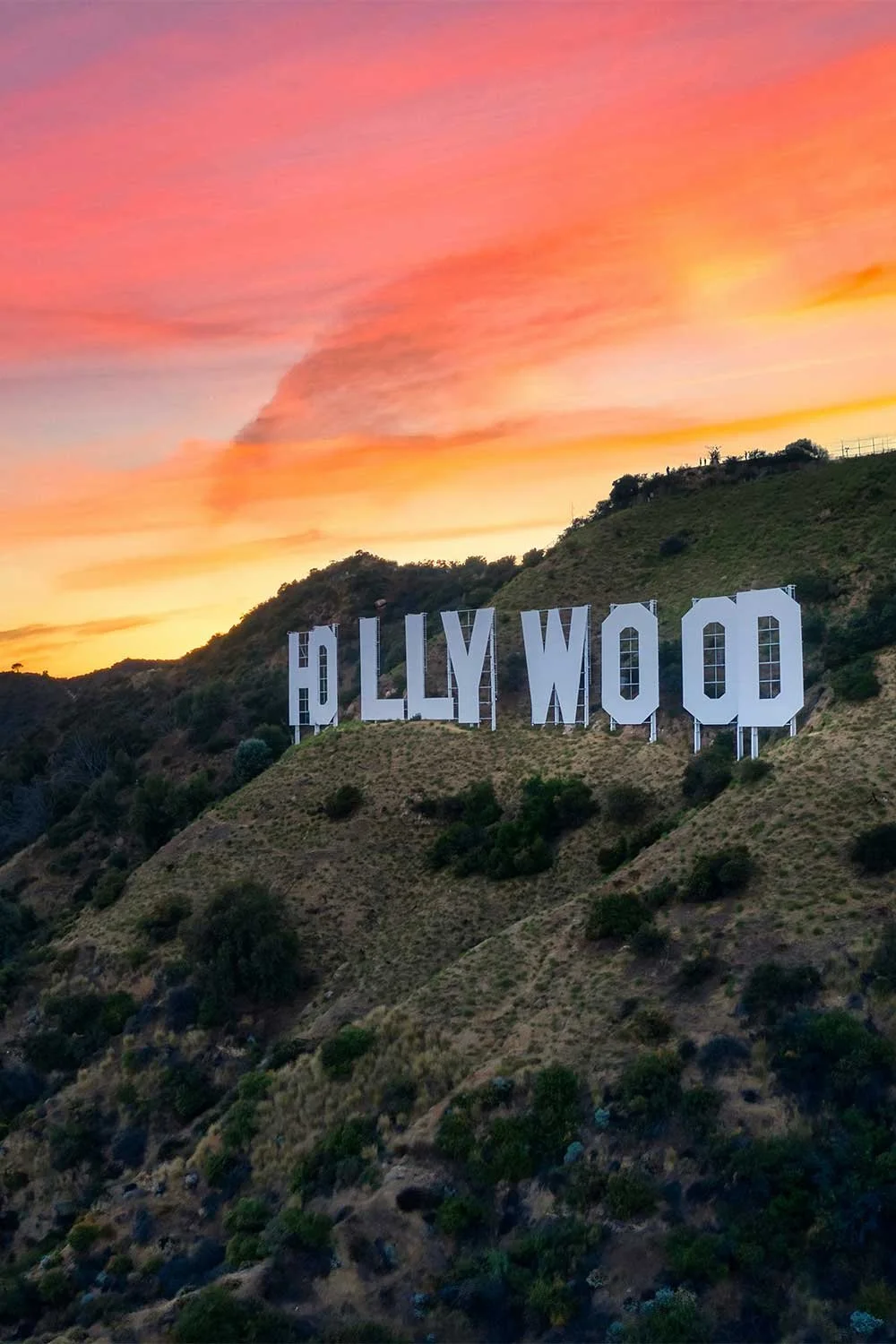 The Hollywood sign on a hillside with a colorful sunset sky in the background.