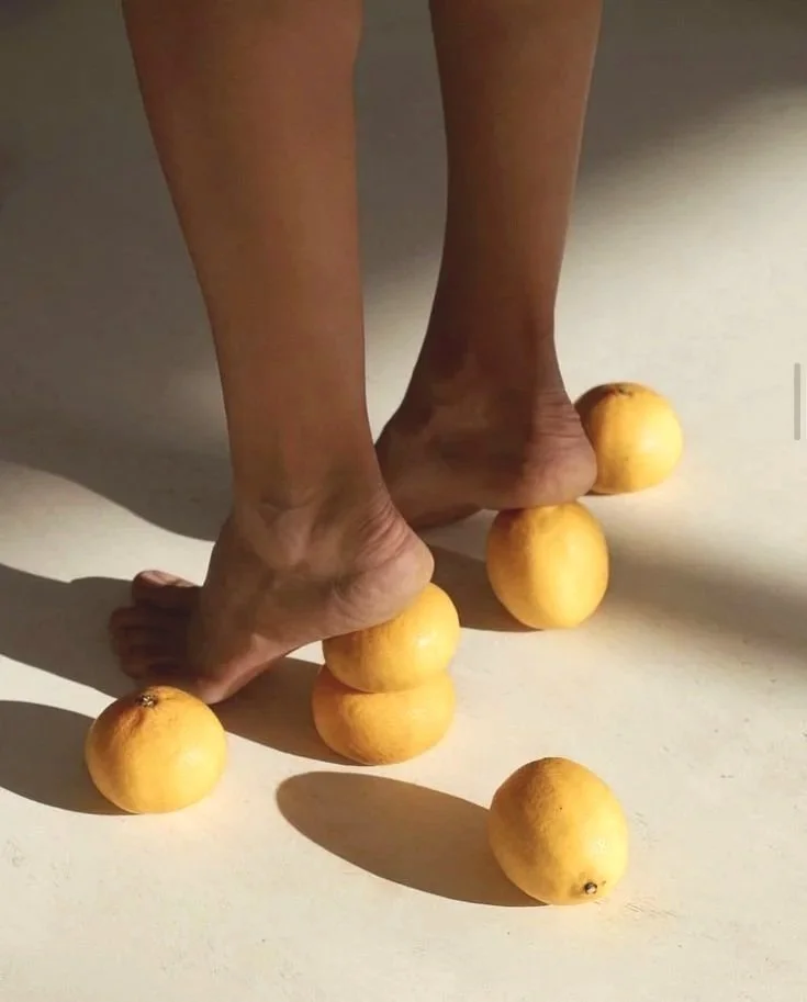 A person's feet standing on an uneven surface made of stacked lemons, with some lemons scattered on the floor around them.
